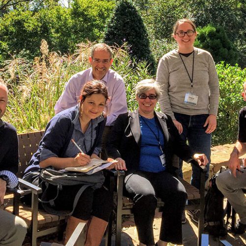 Original HuMetrics Team sitting outside on a patio at the Rizzo Center in Chapel Hill, NC. From left to right is Jason Rhody, Nicky Agate, Chris Long (sitting in the back), Rebecca Kennison, Stacy Konkiel (standing in the back), and Simo Sacchi.