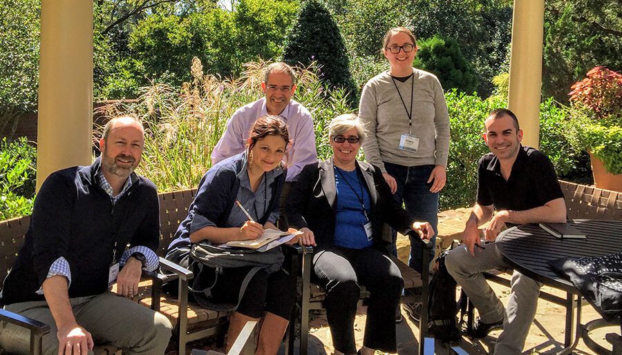 Original HuMetrics Team sitting outside on a patio at the Rizzo Center in Chapel Hill, NC. From left to right is Jason Rhody, Nicky Agate, Chris Long (sitting in the back), Rebecca Kennison, Stacy Konkiel (standing in the back), and Simo Sacchi.