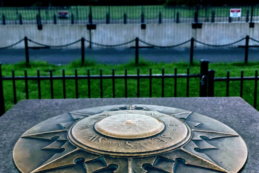 Compass with directions in the foreground with a distant and unfocused image of the White House in the distance.