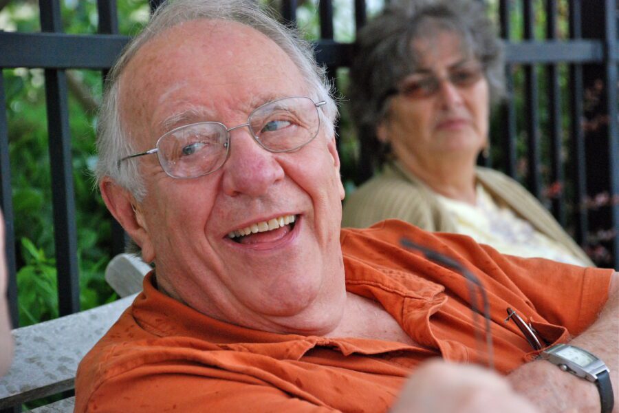 Ted Loder looking to his right with a joyful smile on his face, with Jan Filing, his wife looking on from behind and out of focus.