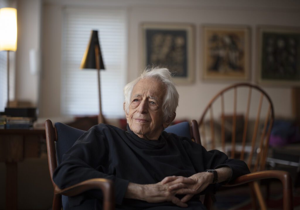 Richard Bernstein, in a black turtleneck, hands folded, with chairs, out of focus, in the background. Bernstein was a champion of democracy and democratic values.