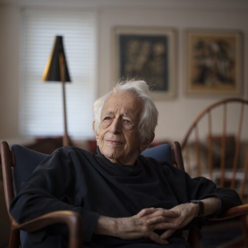 Richard Bernstein, in a black turtleneck, hands folded, with chairs, out of focus, in the background. Bernstein was a champion of democracy and democratic values.