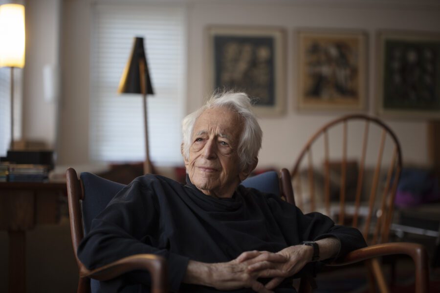 Richard Bernstein, in a black turtleneck, hands folded, with chairs, out of focus, in the background. Bernstein was a champion of democracy and democratic values.