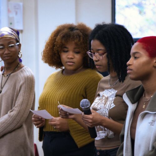 African and African American Studies students standing in a row, from left to right: Amber McAddley, Morgan Braswell, Jhala Martin, and Ayodele Uhuru. They are listening to Jhala read from a piece of paper with a microphone in her hand. Photo by Ryan Frederick.