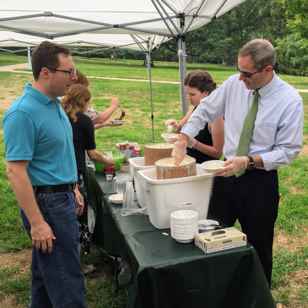 BillHD standing in front of a vat of ice cream in a blue shirt as Chris Long Scoops a bowl of Vanilla for him.